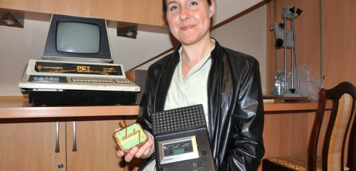 Anna Cieplińska prezentje eksponaty: odtwarzacz kasetowy Unitra i wodę kolońską. Obok, po lewej komputer Commodore