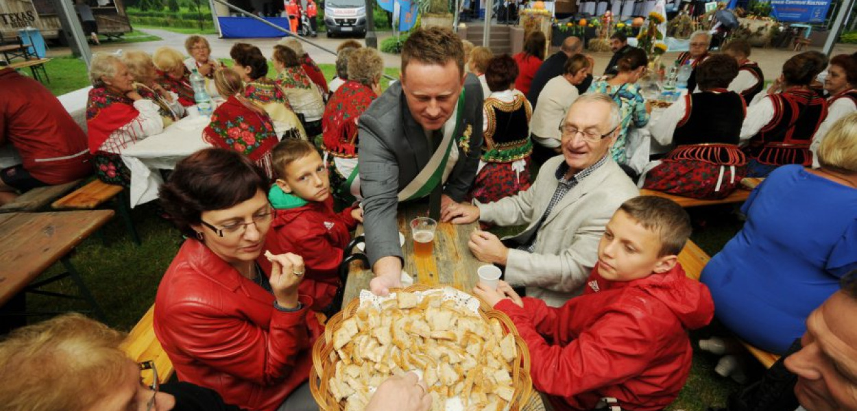 Wiceburmistrz Trzebini Jarosław Okoczuk częstuje mieszkańców dożynkowym chlebem