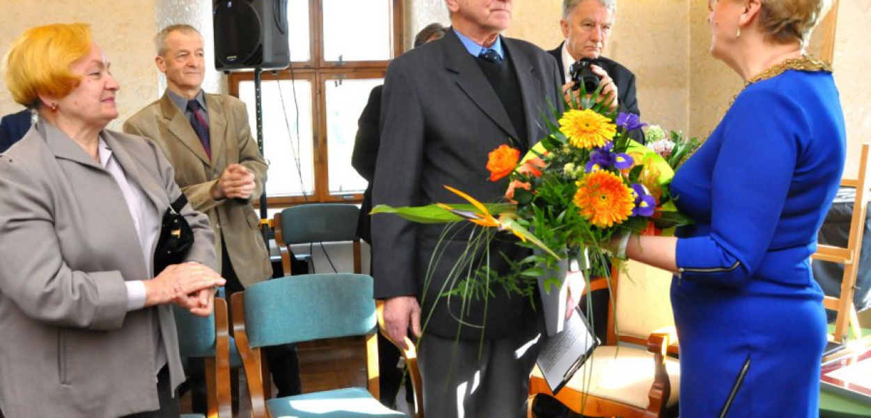 Andrzej Kostka odbiera gratulacje z rąk Grażyny Hrabi, przewodniczącej rady. Towarzyszy mu żona (z lewej)